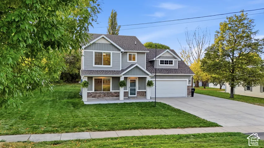 Two-story residence featuring light gray siding, stone accents, a covered front porch, an attached garage, and a concrete driveway