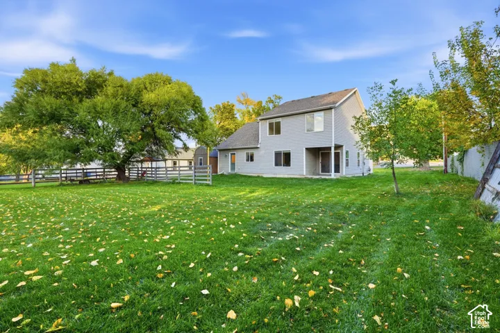 Expansive rear yard with a manicured lawn, established trees, and wood fencing