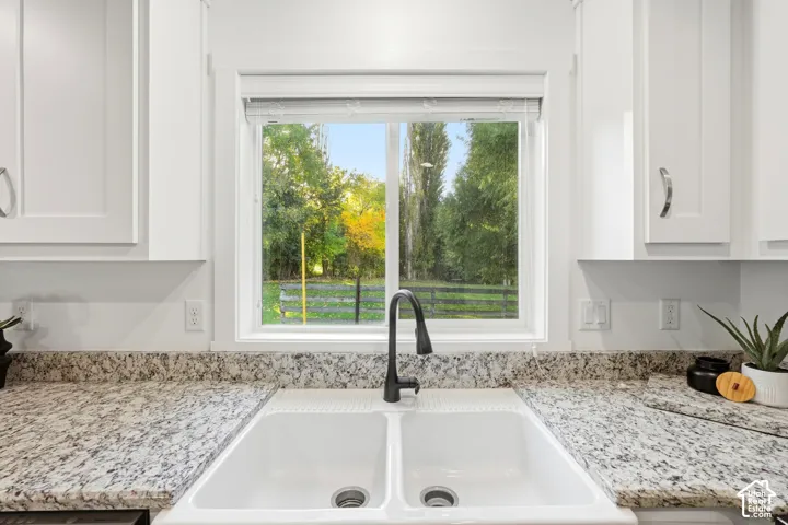 White shaker-style cabinetry with chrome pulls, dual basin apron-front sink with a matte black gooseneck faucet, and speckled light-toned countertops