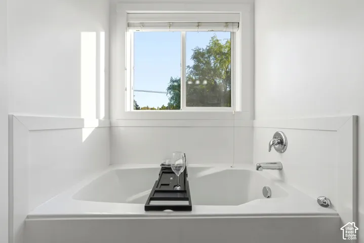 Built-in soaking tub with chrome fixtures, window with natural light, and paneling detailing