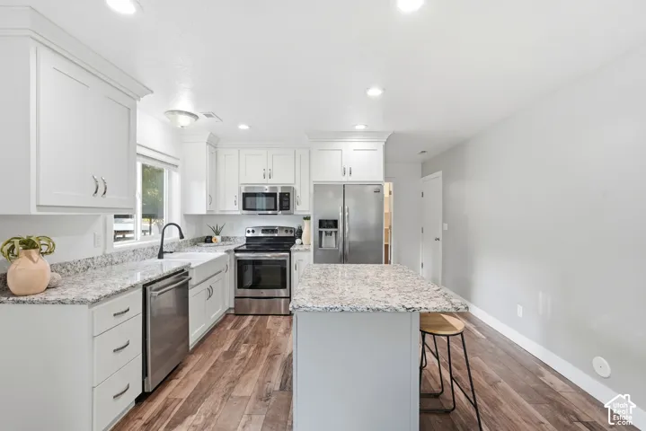 White shaker-style cabinetry, light-colored countertops, stainless steel appliances, wood-finish flooring, and a kitchen island with seating