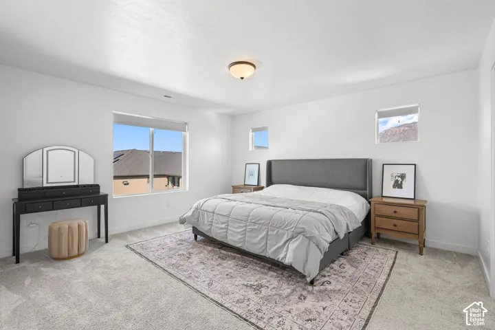 Spacious bedroom featuring light-colored carpeting, multiple windows providing natural light, and a ceiling-mounted light fixture
