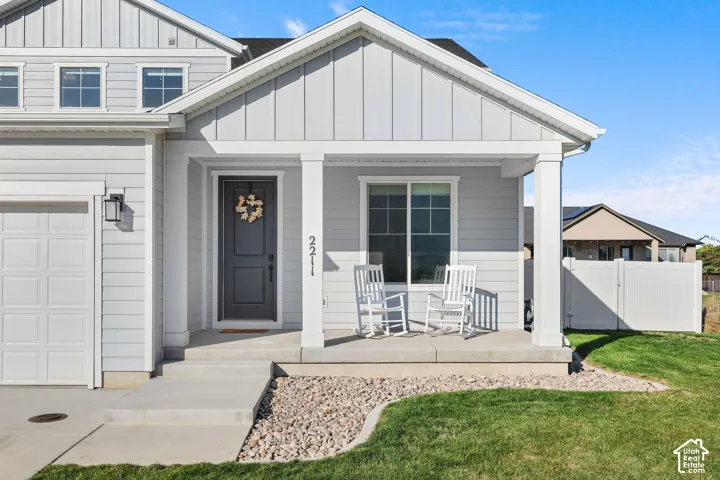 Light gray siding exterior with a covered entry, an attached garage, and a white privacy fence