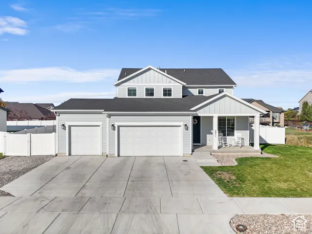 Light gray siding exterior with a covered front porch, two-car garage, concrete driveway, and front lawn