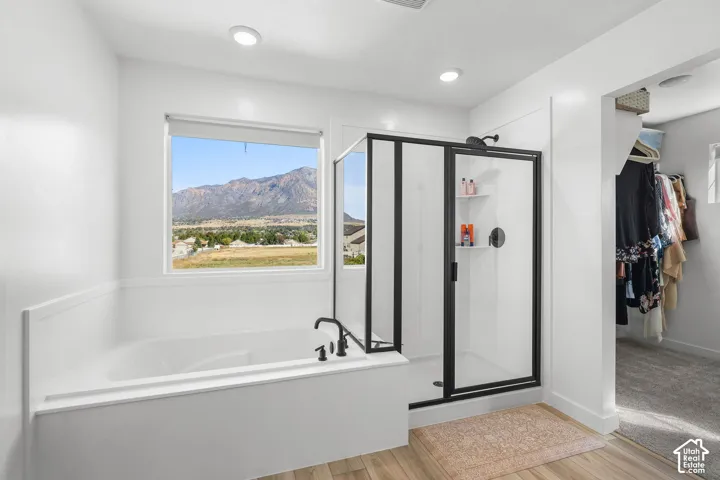 Recessed lighting illuminates the space, featuring a built-in soaking tub, a separate shower with a black-framed glass enclosure, and wood-finish flooring