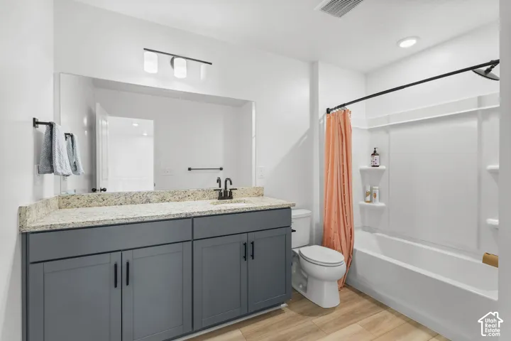 Dual-sink vanity with a granite-style countertop, wood-finish flooring, and a shower-tub combination with built-in shelving