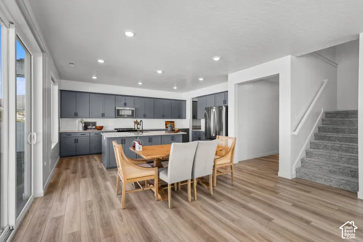 Open-concept kitchen with wood-finish flooring, dark-toned cabinetry, stainless steel appliances, and recessed lighting