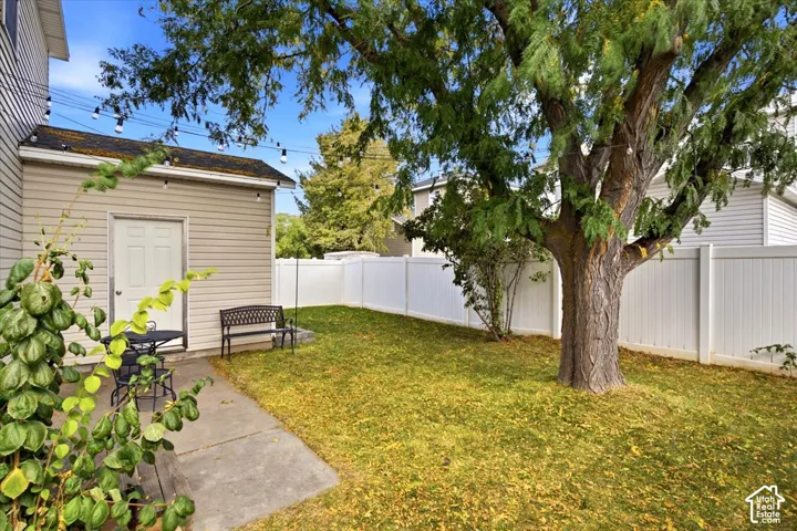 Beautiful backyard featuring a mature shade tree, manicured lawn, and white vinyl privacy fencing