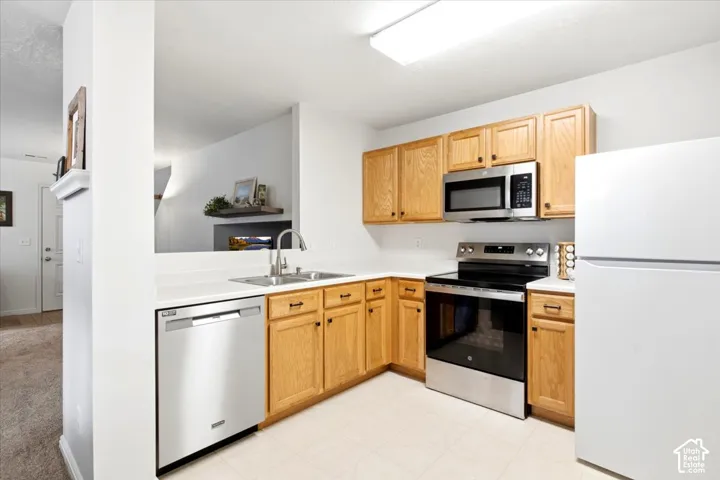 Kitchen with light wood-finish cabinetry, white countertops, and stainless steel appliances including a dishwasher, range, and microwave