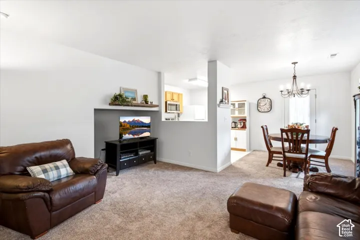 Carpeted living area with a built-in display shelf, a dining area featuring a chandelier, and a partial view of the kitchen with light wood-finish cabinetry