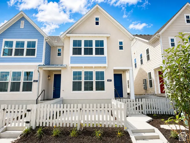 Stucco exterior with blue siding accents, multiple windows, a prominent blue front door, white picket fencing, and a concrete walkway