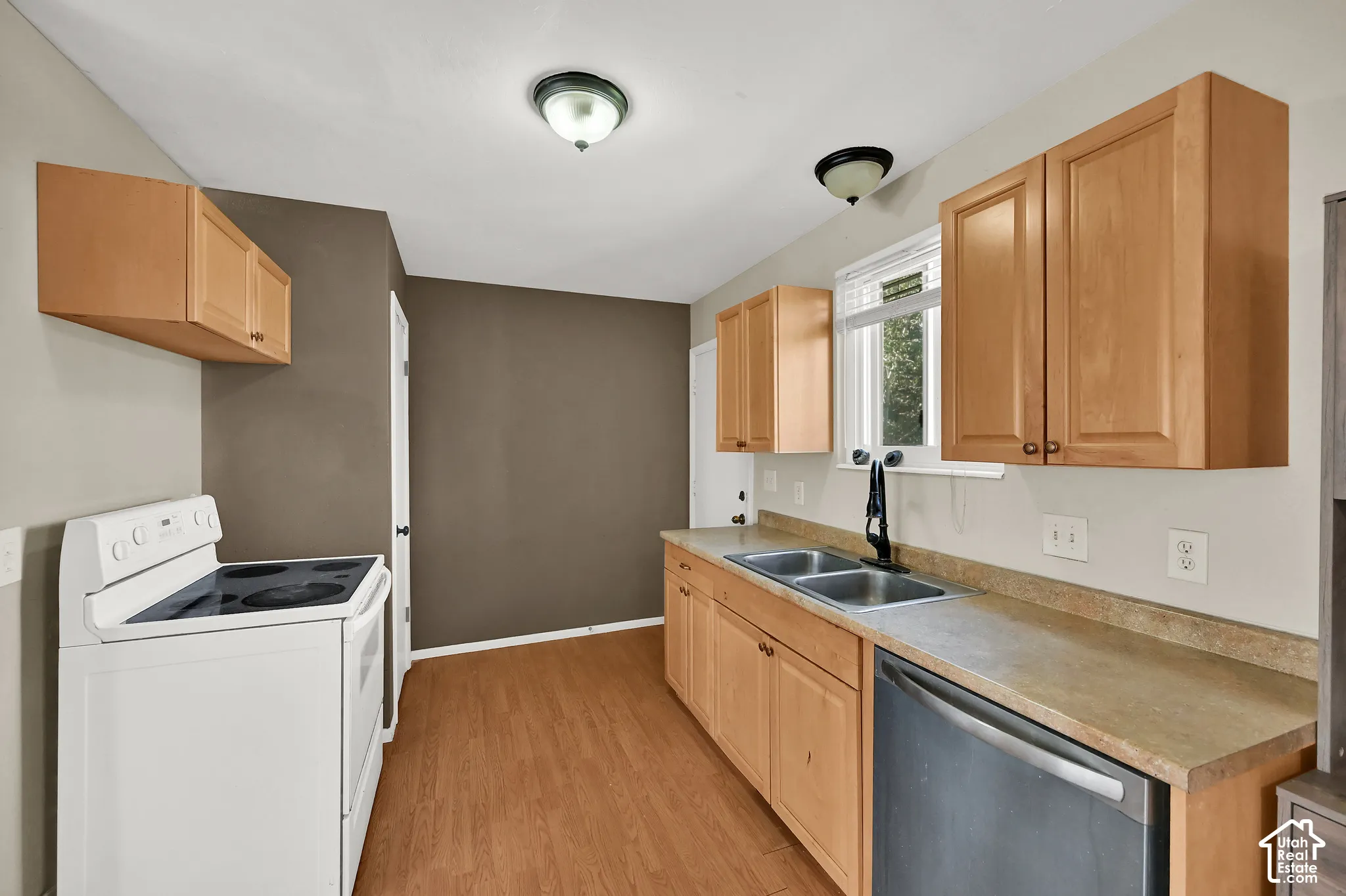 Wood-finish flooring, light wood cabinetry, dual basin sink, stainless steel dishwasher, and a white electric range