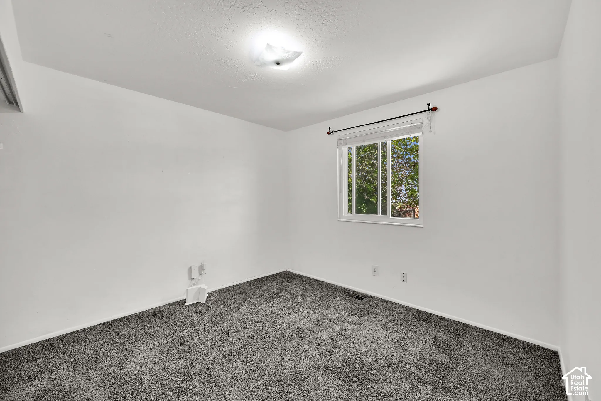 Grey carpeted flooring with white wall finishes, a white-framed window, and a ceiling-mounted light fixture