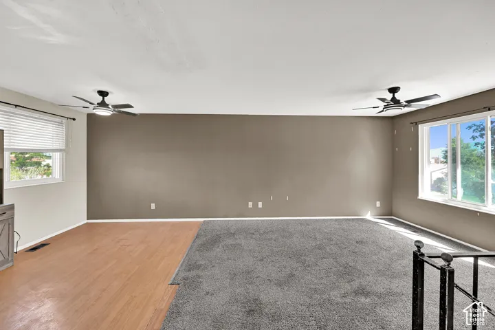 Room featuring mixed flooring with wood-finish and carpeted areas, two windows with blinds, and two ceiling fans with integrated lighting