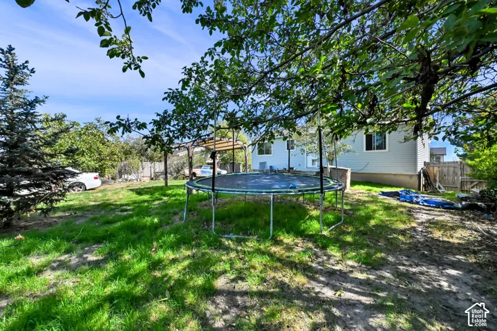 Grassed backyard with mature trees, a privacy fence, and a visible house exterior with light blue siding