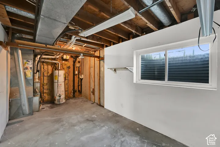Basement space featuring exposed ceiling joists, concrete flooring, a water heater, and a sliding window