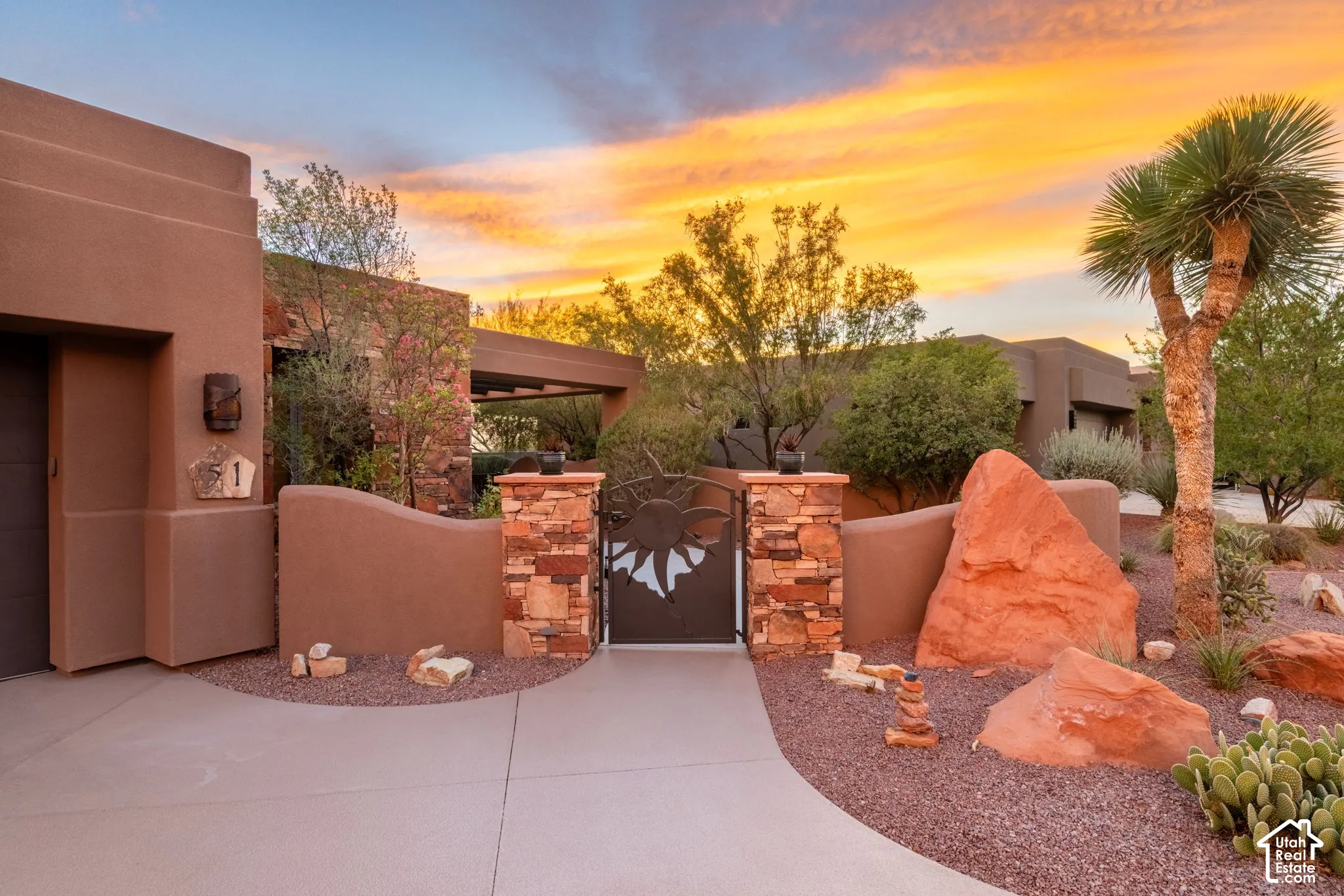 Desert landscaping with natural rock features, stucco exterior, decorative privacy wall, and a wrought iron gate