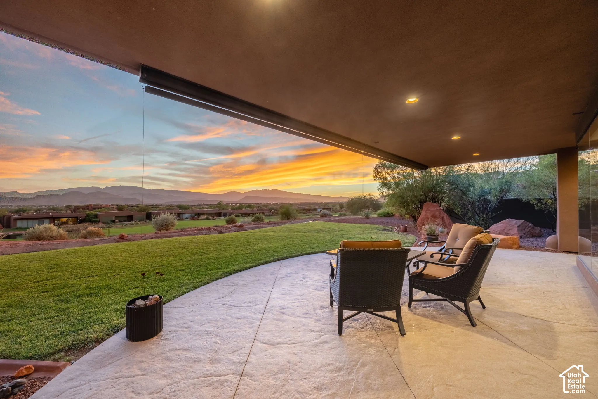 Covered patio with stamped concrete flooring, recessed lighting, expansive lawn, and distant mountains