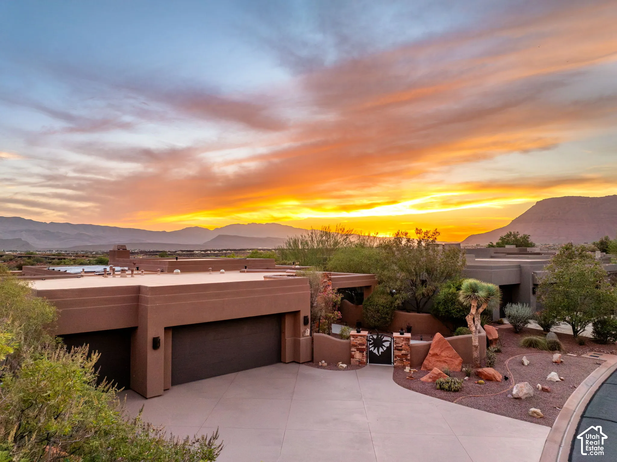 Stucco exterior, two-car garage, mature desert landscaping, paved driveway, and mountain scenery
