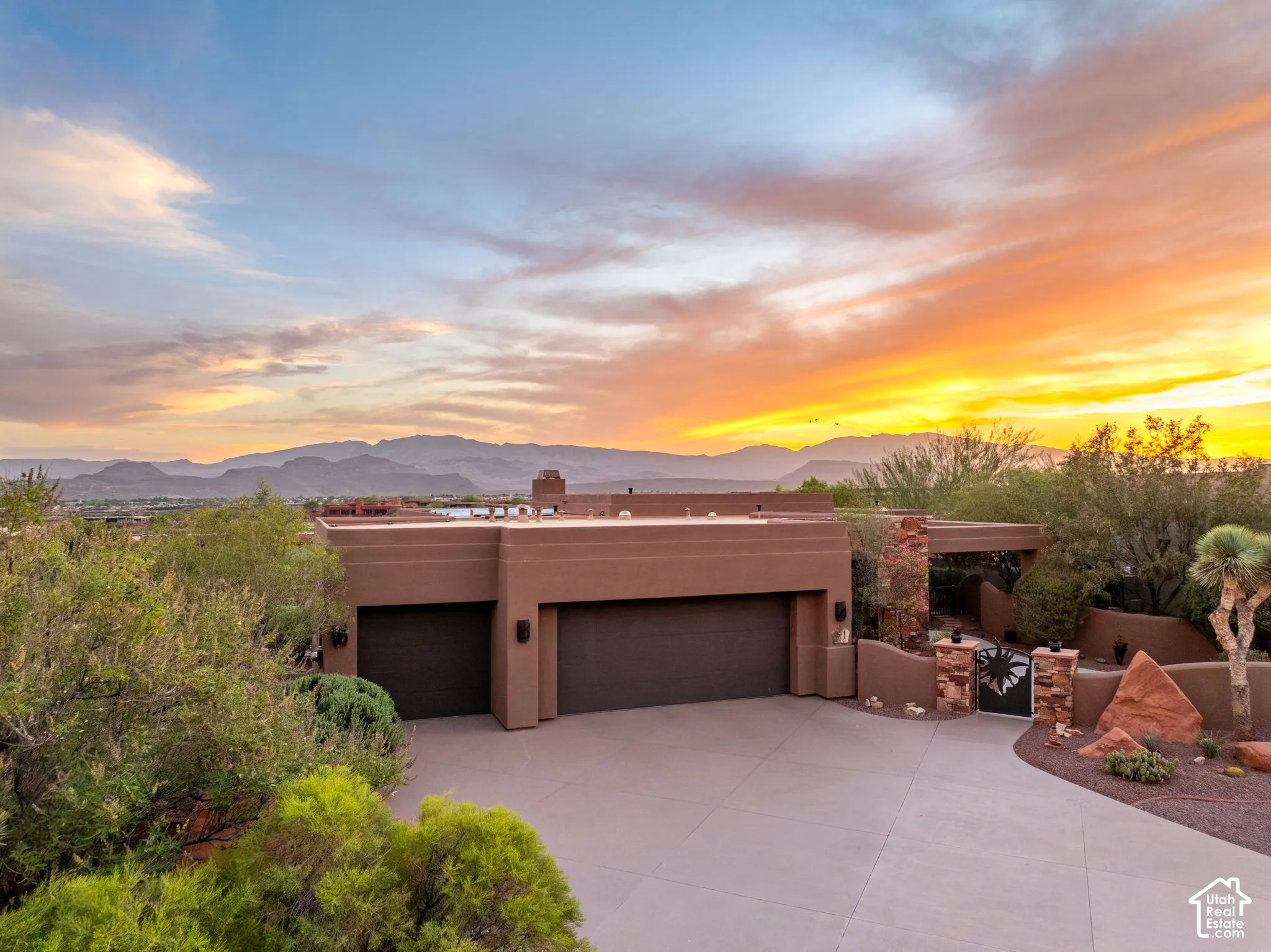 Desert contemporary architecture with an expansive driveway, attached two-car garage, and a gated stone entry