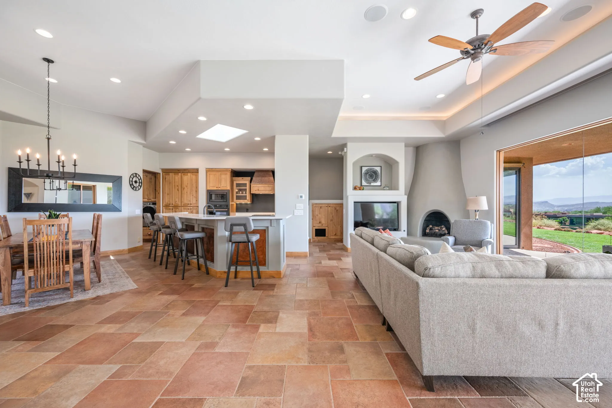 Open-concept living space featuring expansive tile flooring, a built-in fireplace, a large kitchen island with seating, and a dining area with a chandelier