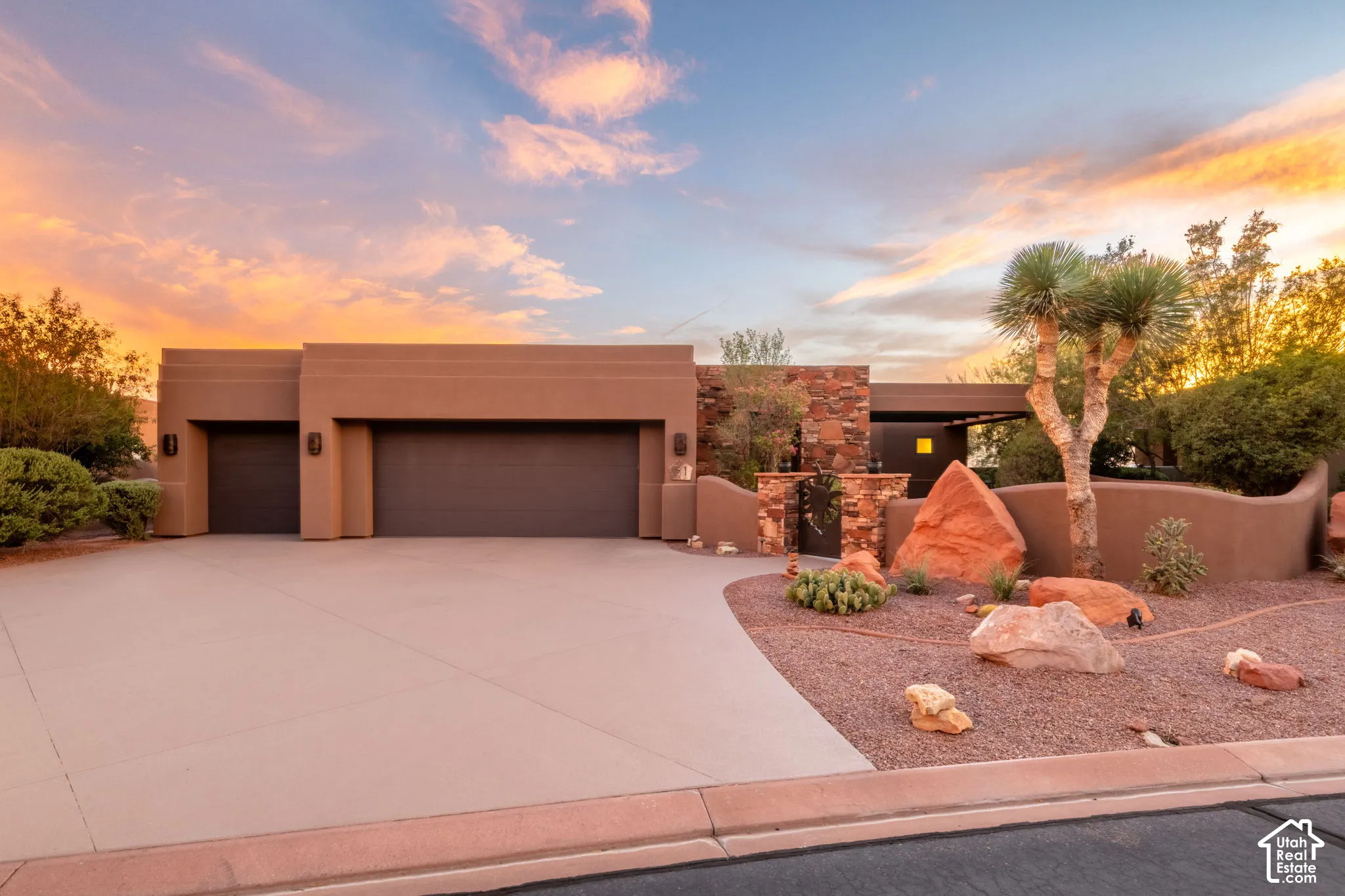 Stucco exterior with a multi-car garage, concrete driveway, stone accents, and desert landscaping