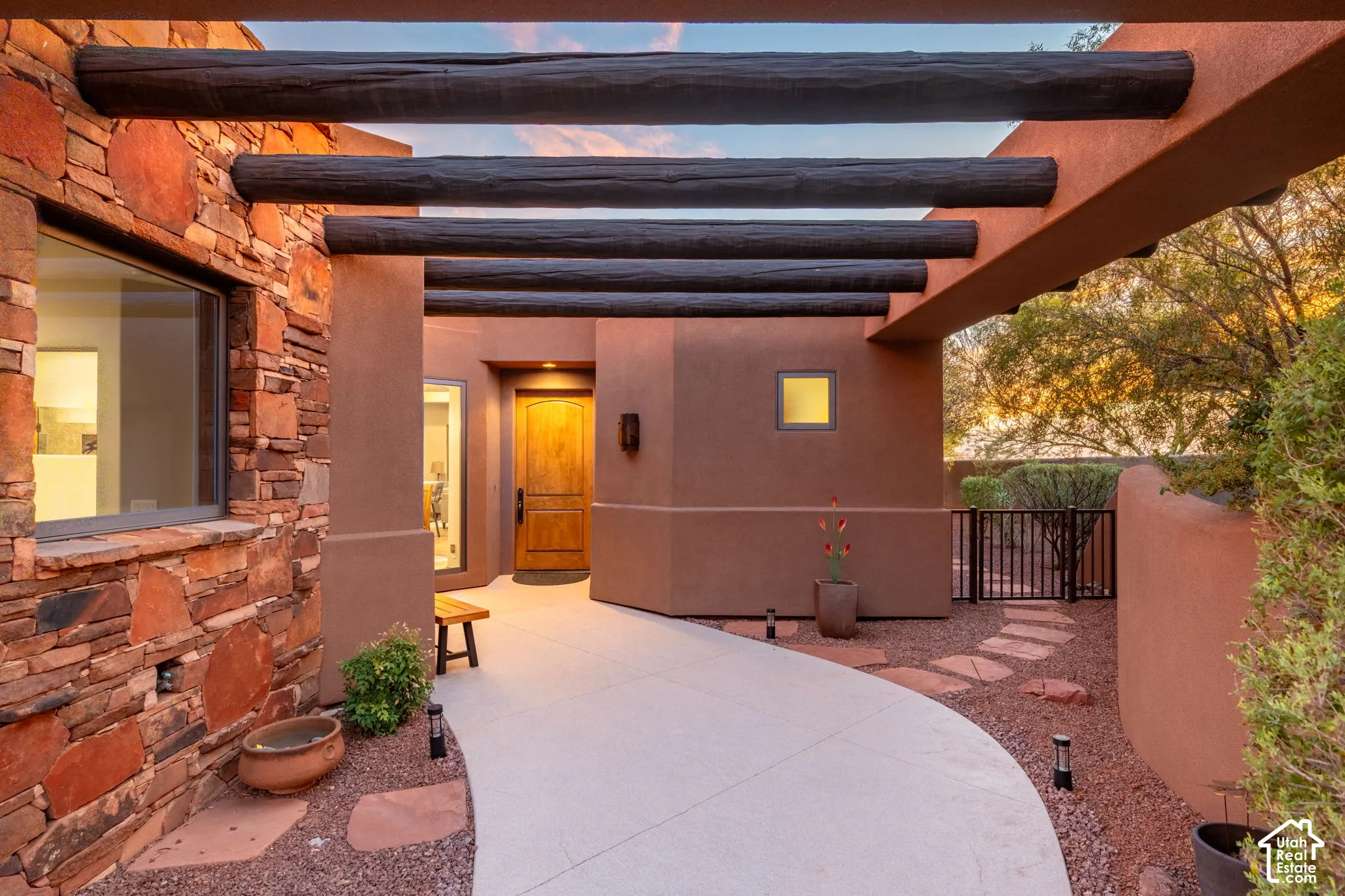 Stucco exterior with stone accents, exposed wooden beams, a wrought iron gate, and a curved concrete pathway