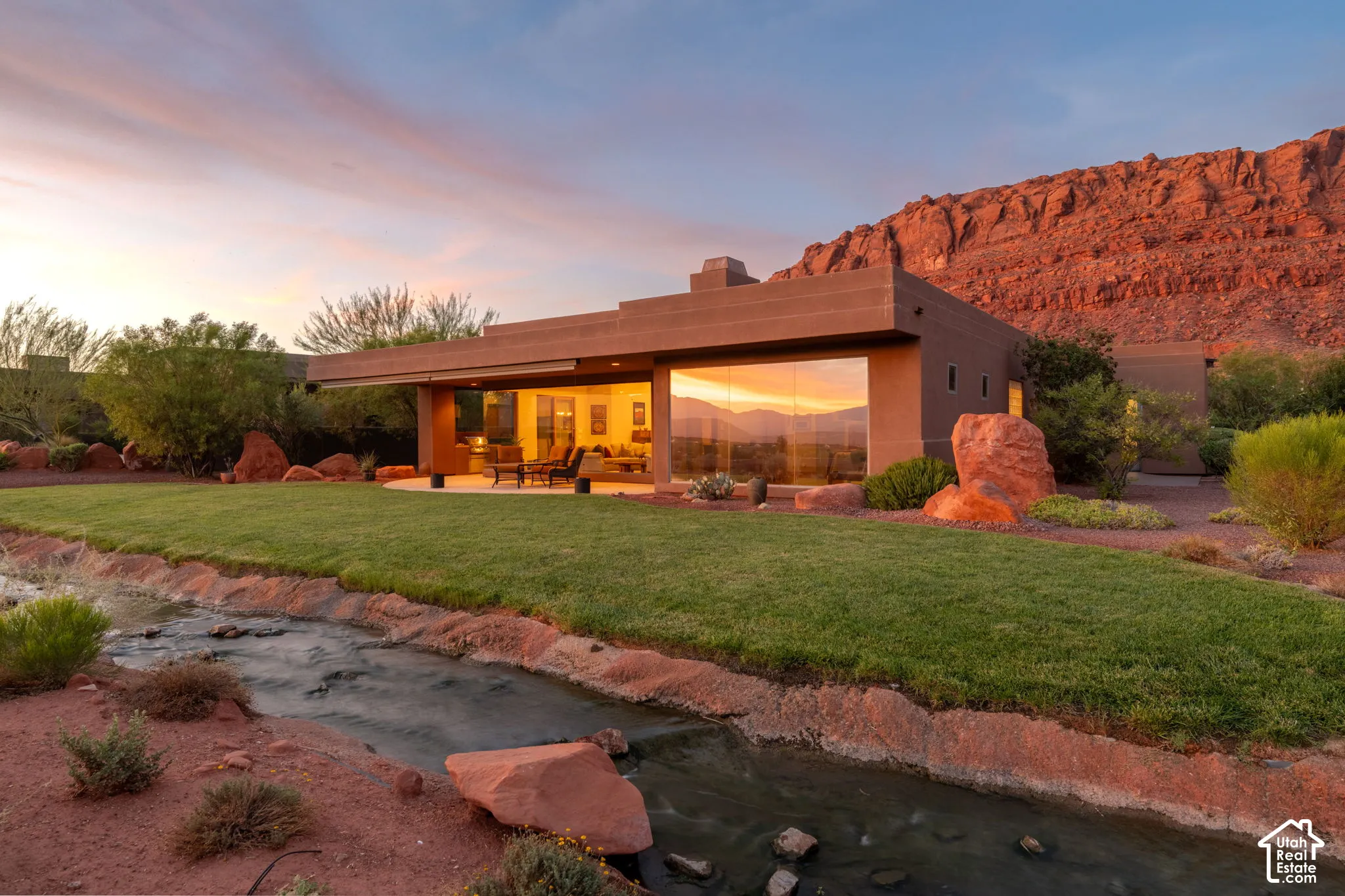 Stucco exterior with extensive window walls, an outdoor covered patio, and a manicured lawn