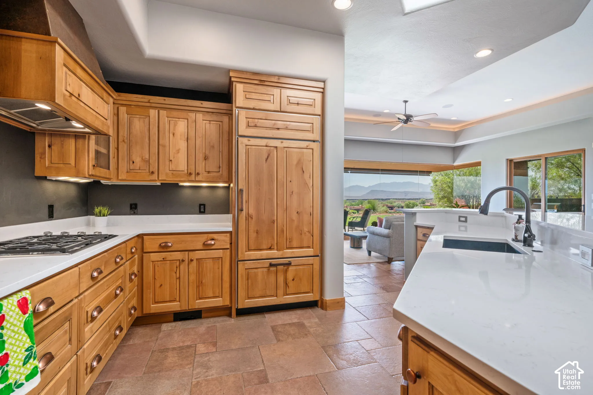 Wood cabinetry, white countertops, stainless steel gas cooktop, integrated refrigerator, and a kitchen island with an undermount sink