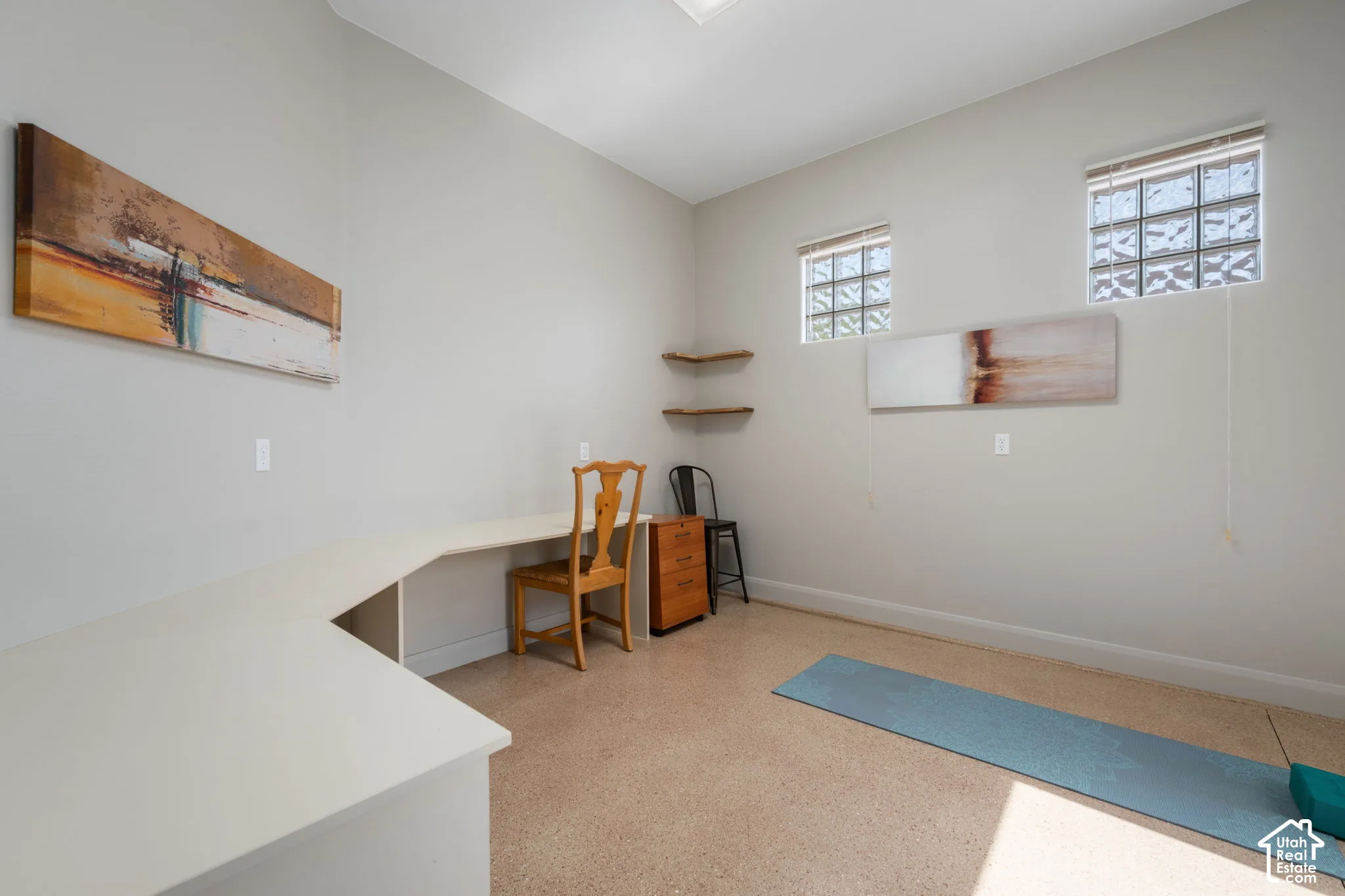 Built-in wraparound desk with neutral-toned countertop, two inset glass block windows, two corner floating shelves, and carpet flooring
