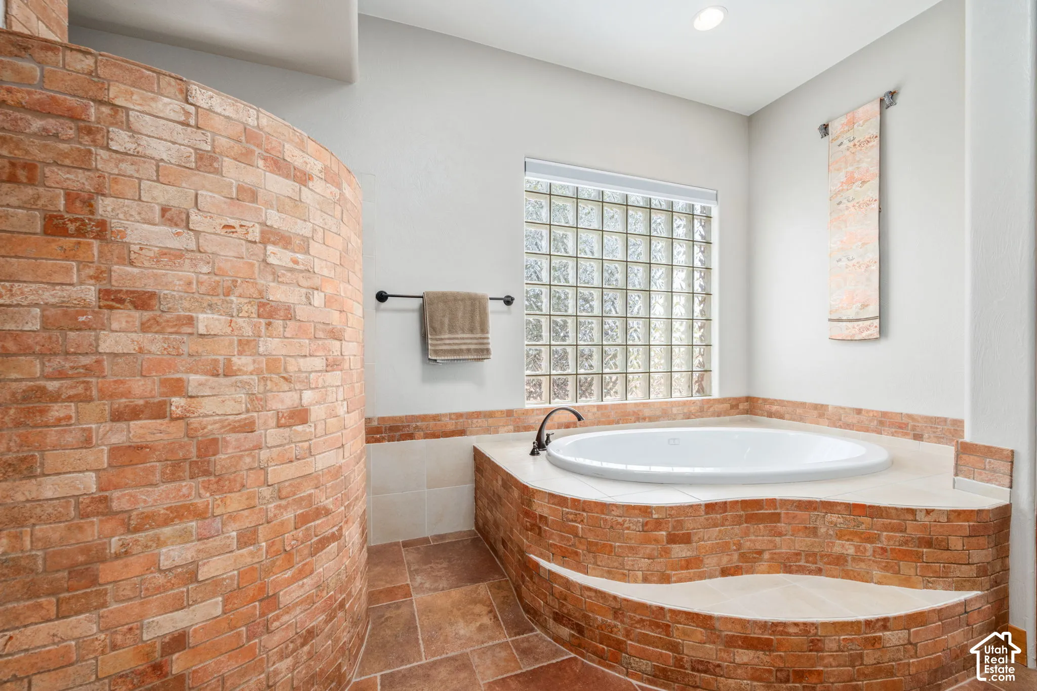 Built-in soaking tub with brick surround, glass block window, recessed lighting, and tile flooring