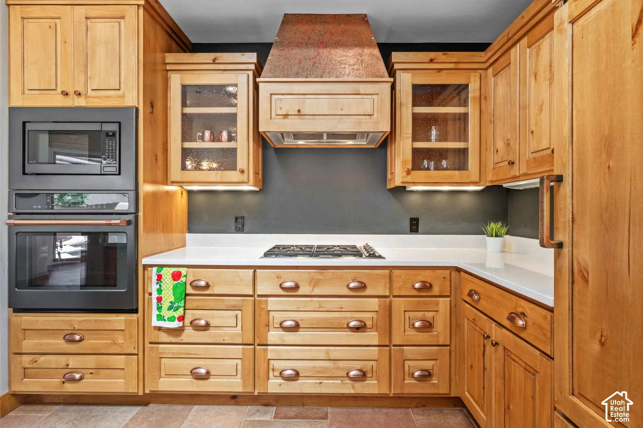 Custom wood cabinetry with glass-front accents, built-in microwave and oven, a gas cooktop, white countertops, and a copper range hood