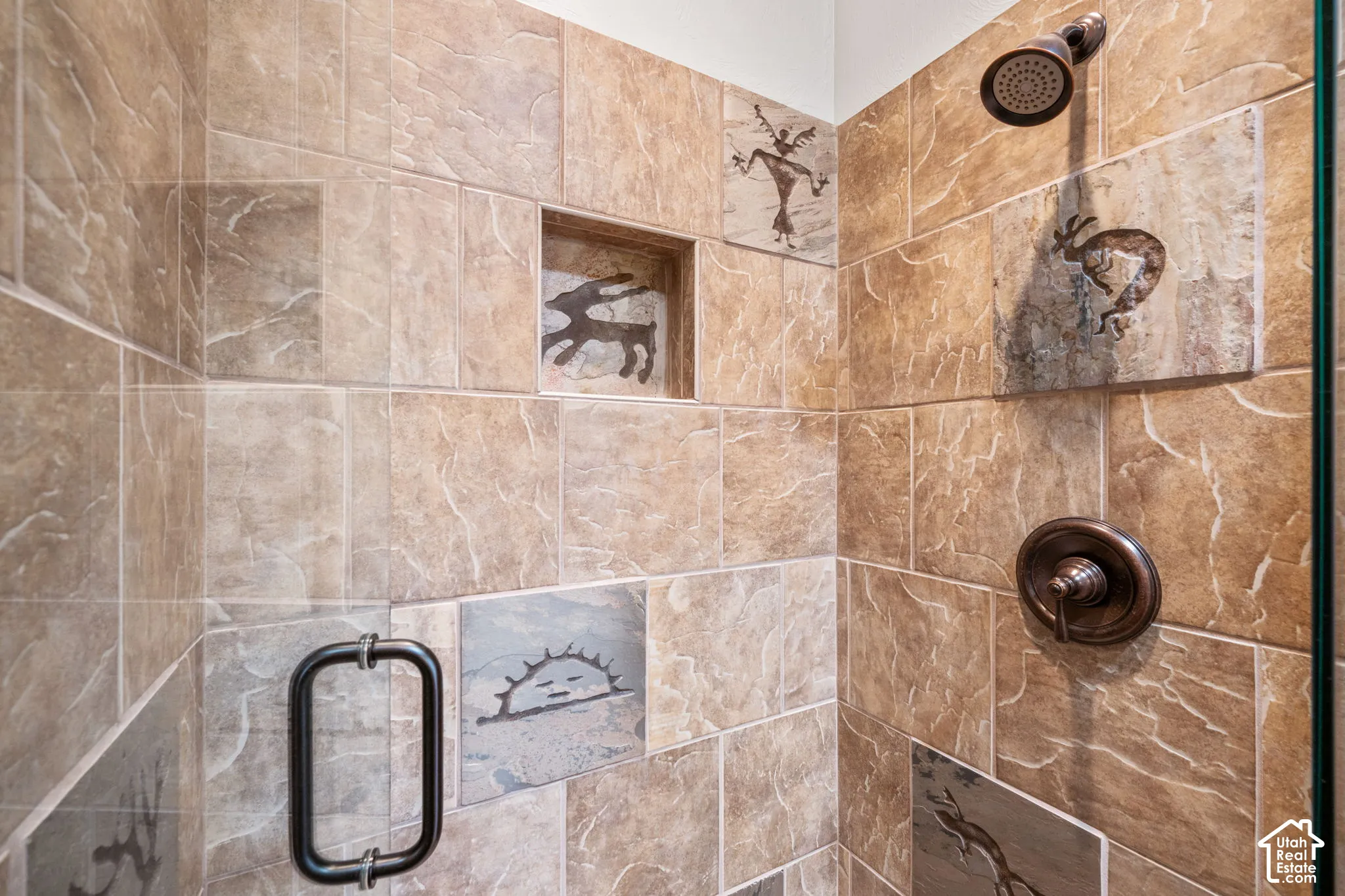 Tiled shower enclosure featuring a built-in niche, decorative accent tiles, bronze-finish shower head, and bronze-finish handle