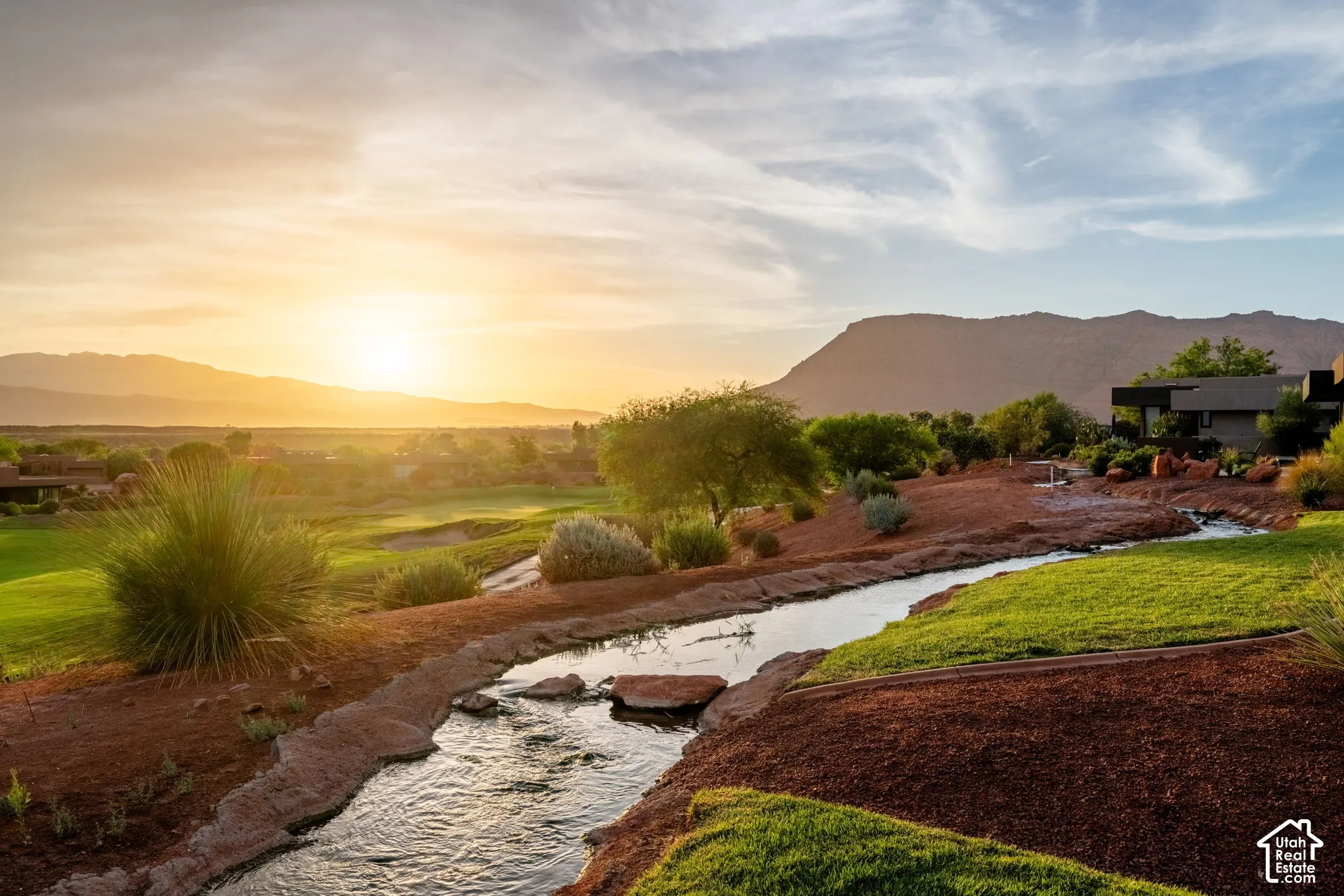 Manicured green spaces, natural rock-lined water feature, rugged mountain backdrop, and expansive natural scenery