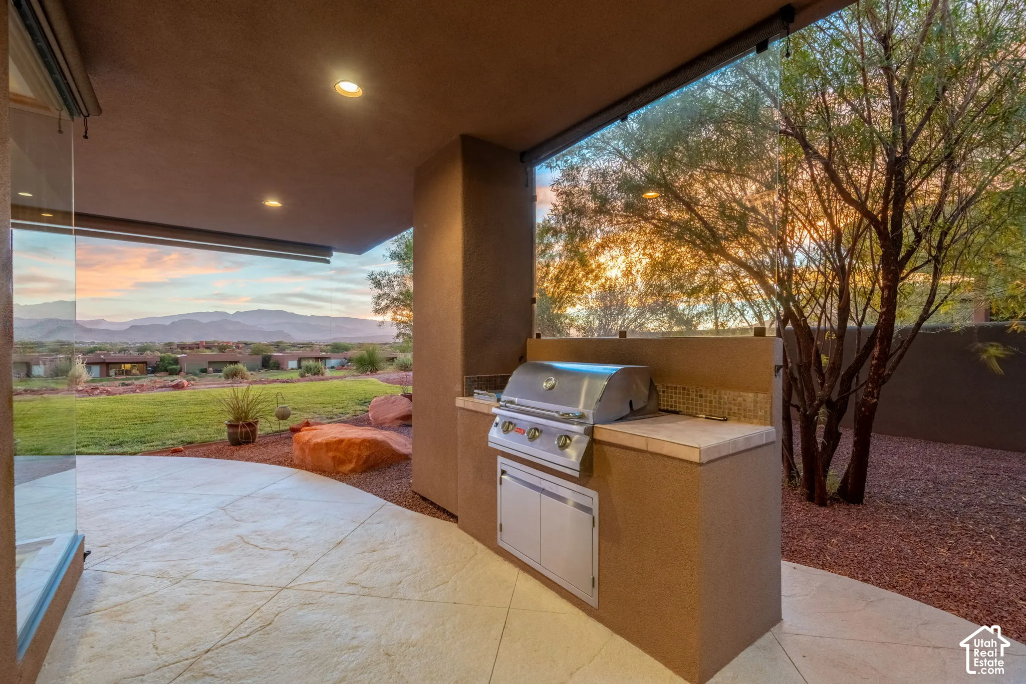 Covered patio with recessed lighting, stone-finish flooring, and an integrated outdoor kitchen featuring a built-in grill and tile backsplash