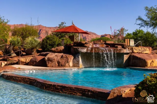 Swimming pool featuring a rock waterfall, surrounded by natural stone hardscaping, lush desert landscaping, and distant mountain scenery