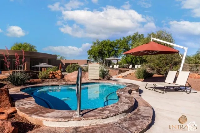 Resort-style pool area featuring a built-in spa with stone surround, a concrete pool deck, and mature landscaping