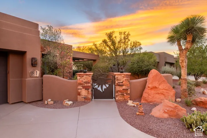 Desert landscaping with natural rock features, stucco exterior, decorative privacy wall, and a wrought iron gate