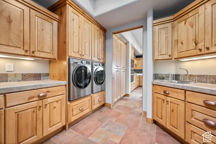 Extensive wood cabinetry, stone tile flooring, built-in stainless steel washer and dryer, countertop, and a utility sink
