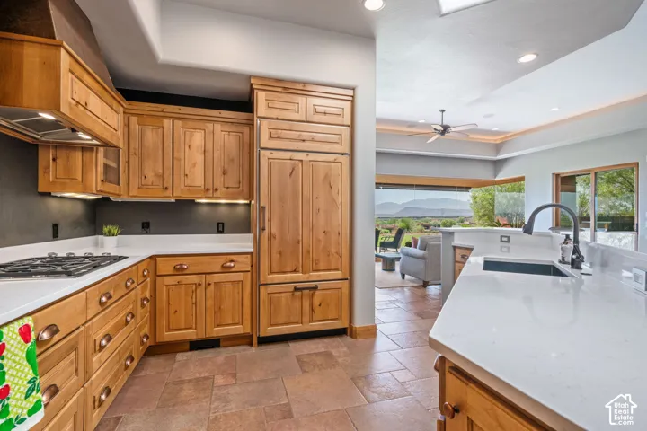 Wood cabinetry, white countertops, stainless steel gas cooktop, integrated refrigerator, and a kitchen island with an undermount sink