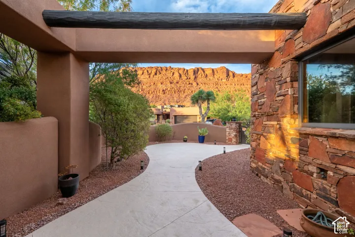 Stucco exterior with a rustic wood beam accent, natural stone facade, curved concrete pathway, and desert landscaping