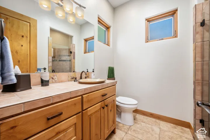 Wood-finish vanity with a tile countertop, vessel sink, and wall-mounted light fixture