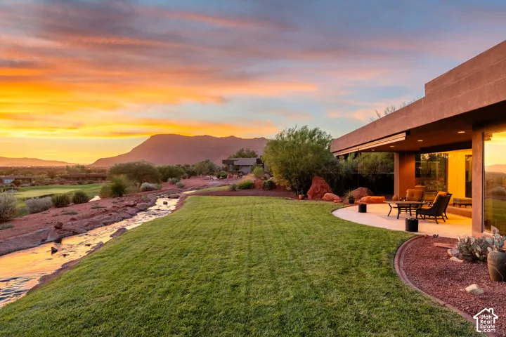 Curved patio with a covered outdoor living area, expansive lawn, and natural water feature