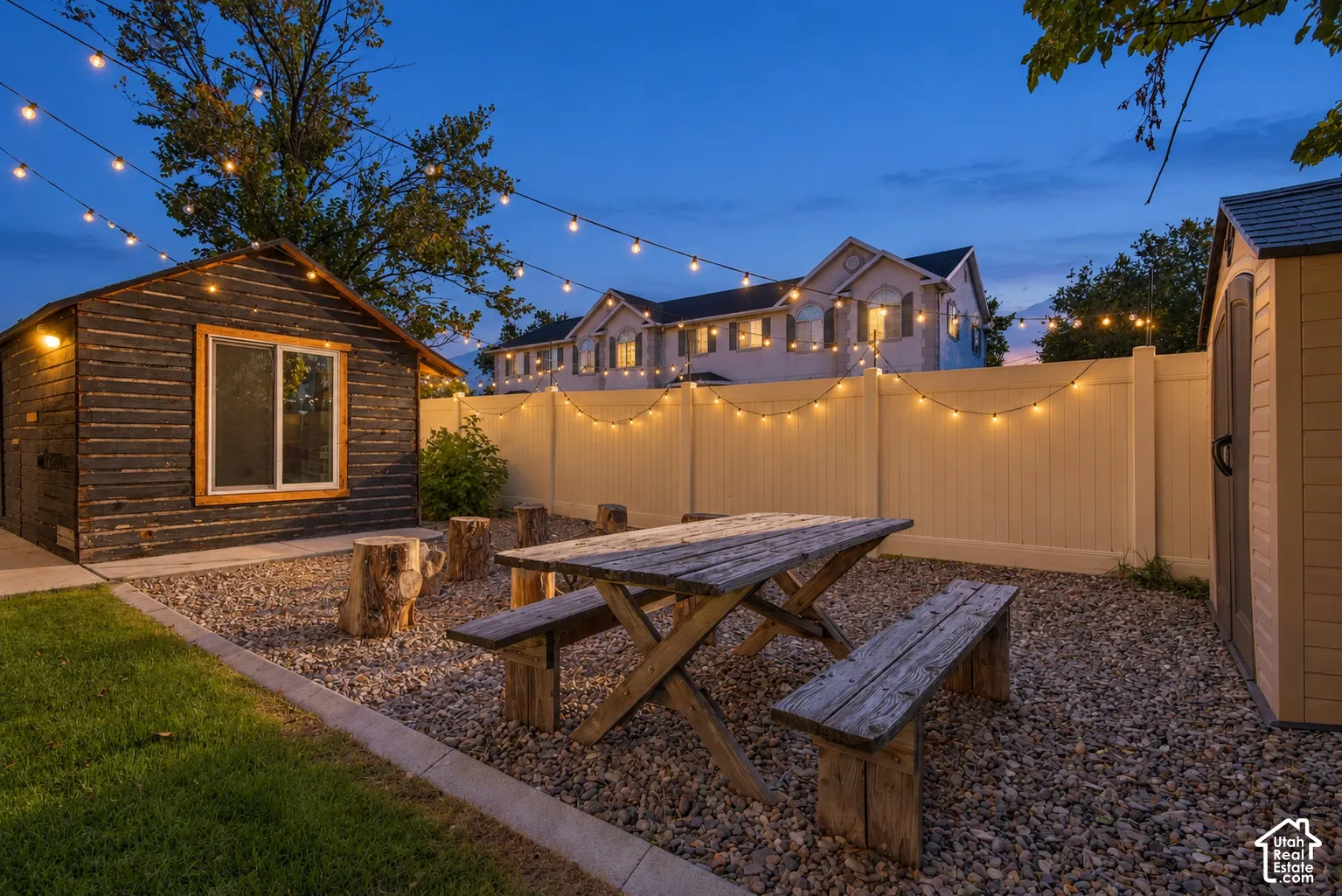 Detached wood-clad accessory structure with window, gravel ground cover, wood picnic table, and composite privacy fencing