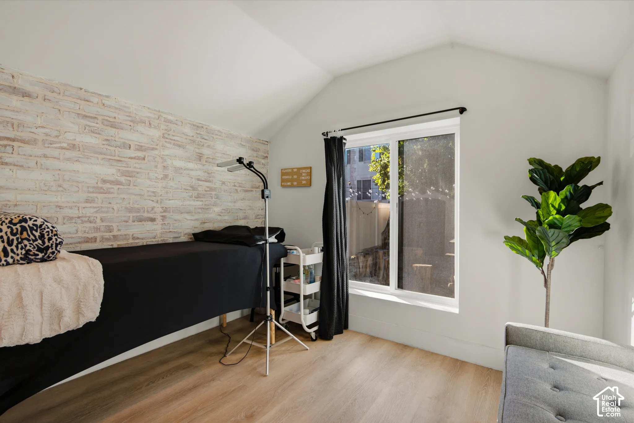 Vaulted ceiling, distressed brick-finish accent wall, wood-finish flooring, and white painted walls