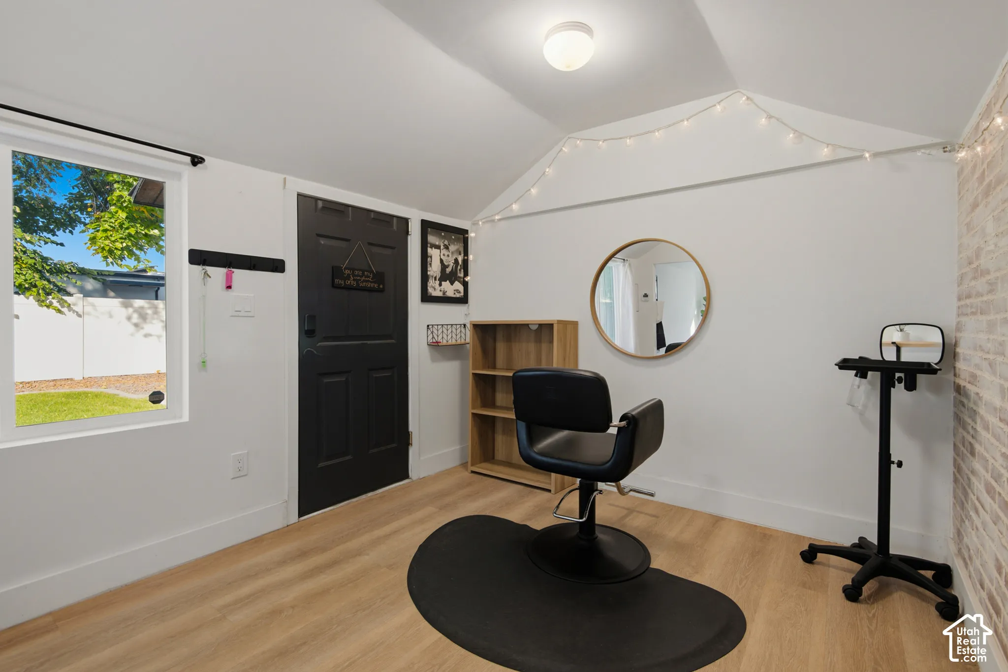 Wood-finish flooring, white painted walls, a vaulted ceiling, and a window providing natural light
