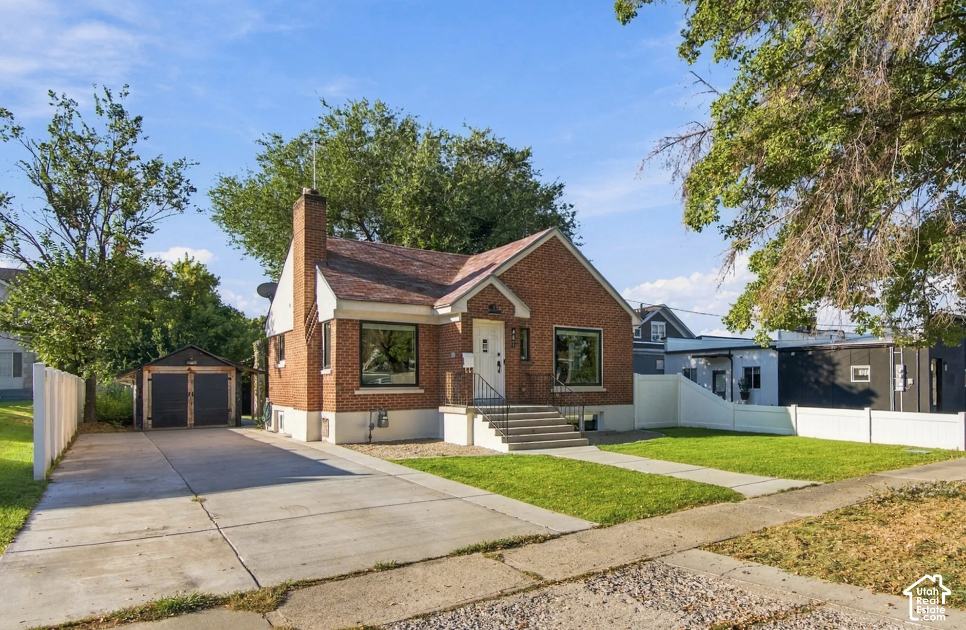 Brick exterior with a prominent chimney, concrete driveway, detached two-car garage, and a manicured lawn