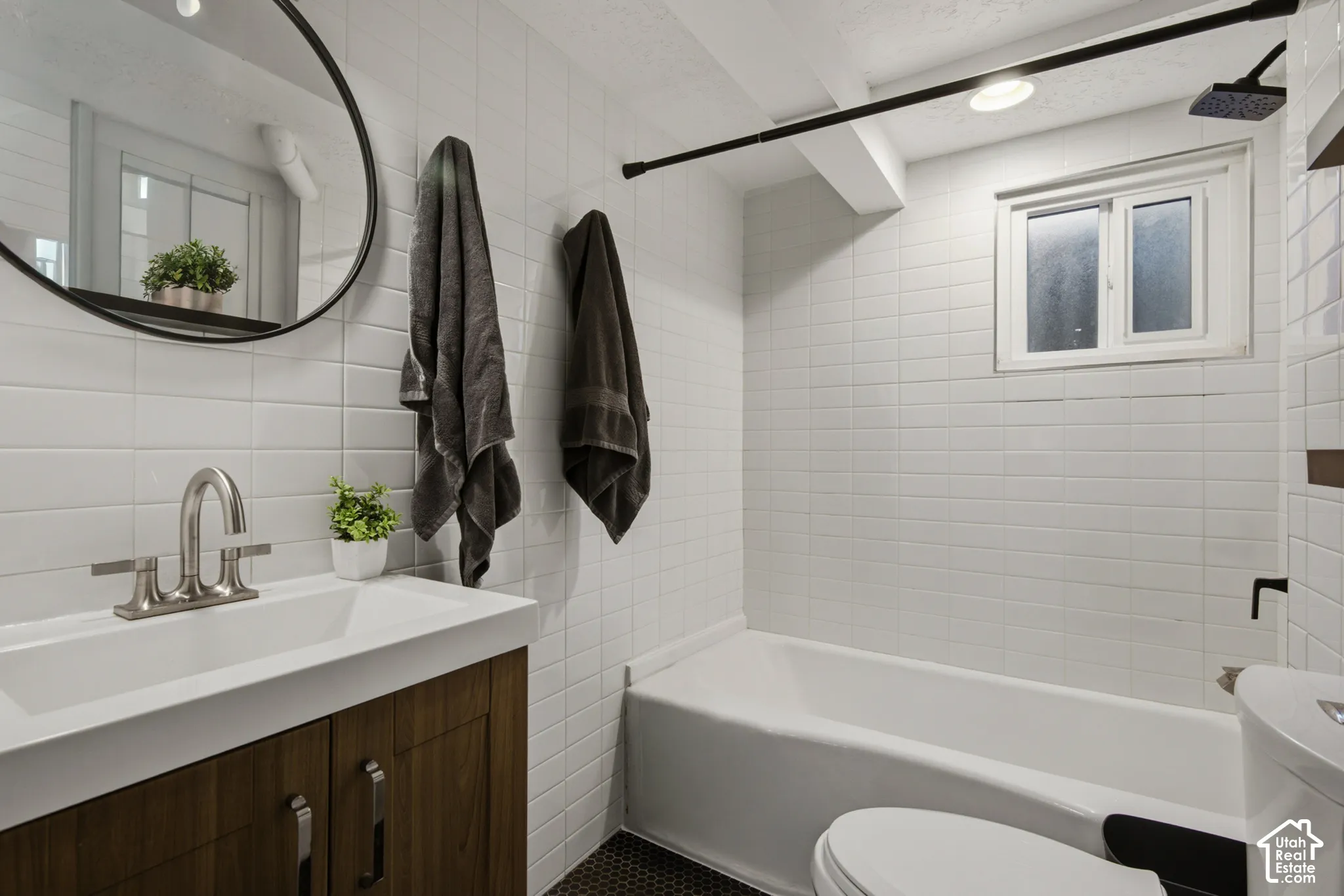 White subway tile walls, wood-finish vanity with integrated sink, brushed nickel faucet, deep soaking tub, and black hexagonal floor tiles