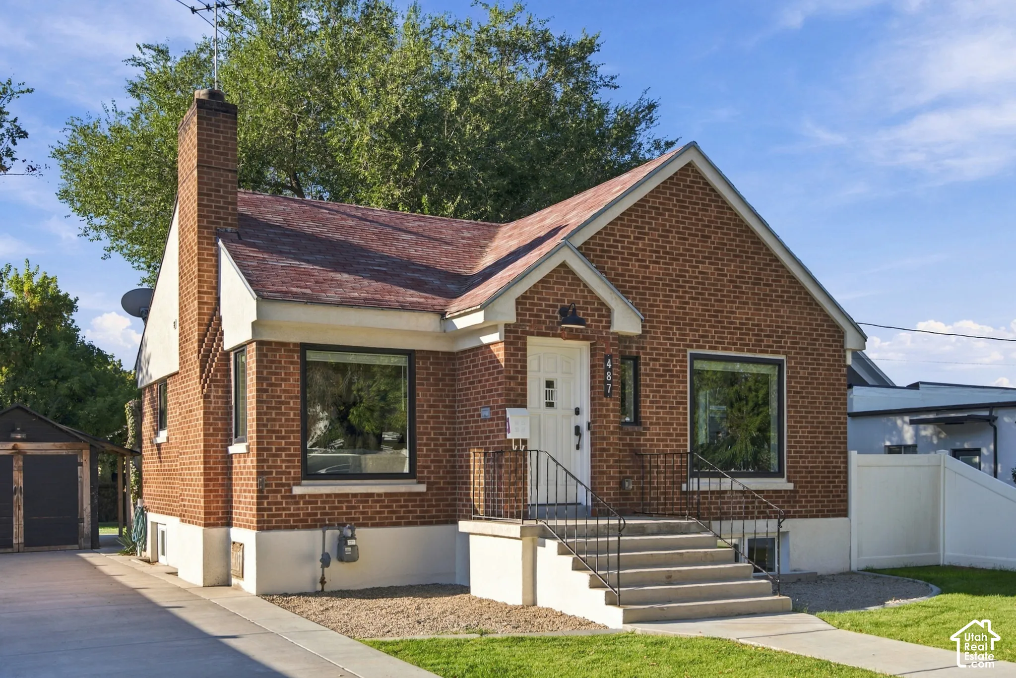 Brick exterior with a prominent chimney, concrete front steps with wrought iron railings, and a side driveway leading to a detached structure