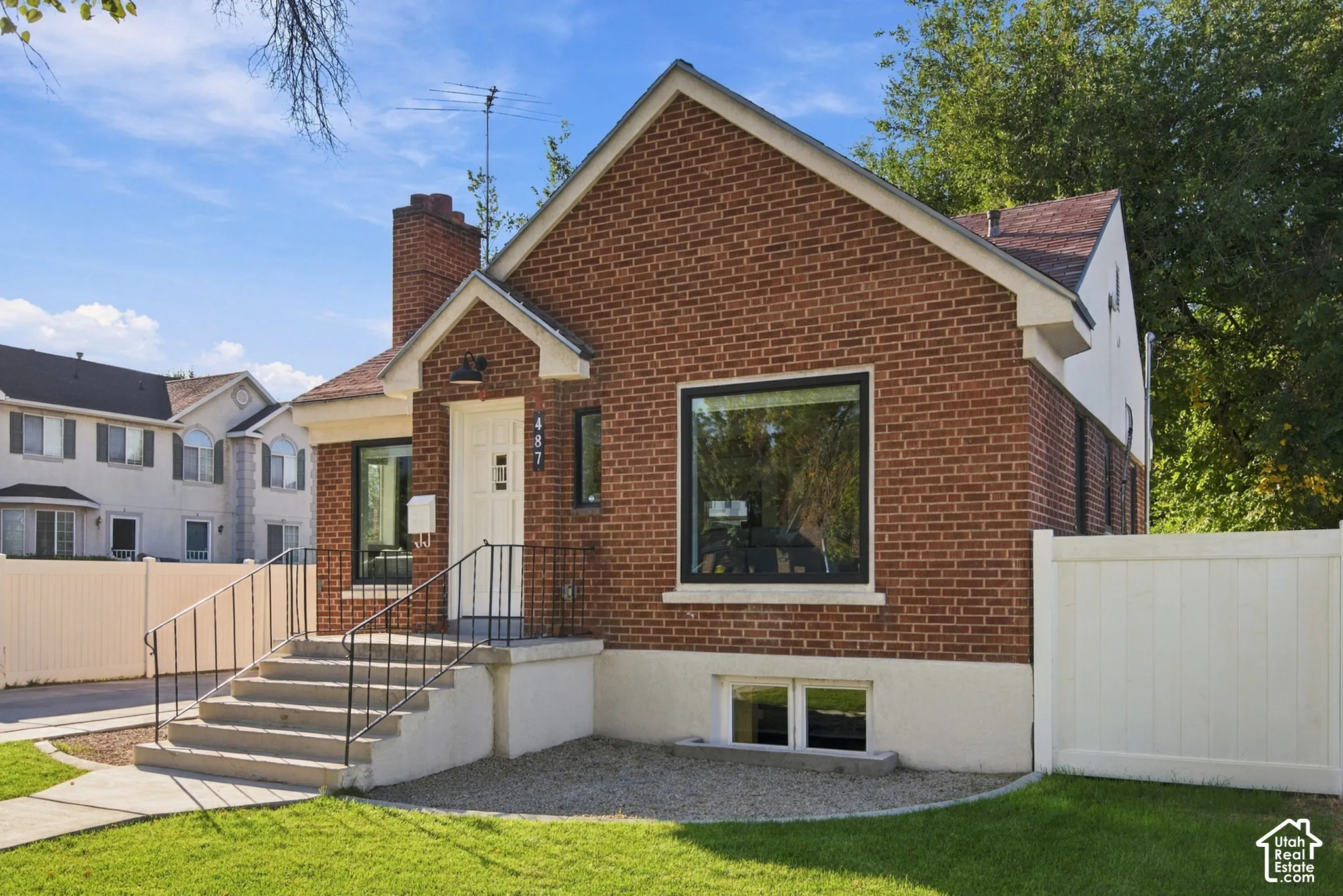 Brick exterior, pitched roofline, white vinyl fencing, concrete steps with wrought iron railing, manicured lawn